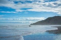 A pair of surfers walking into breaker water at Makorori Beach, mist rising over water obscuring distant mountains