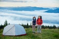 Pair of tourists with backpacks near tent against blurred background mighty mountains