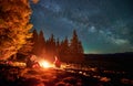 Two tourists resting by fire during night camping in mountains. Royalty Free Stock Photo