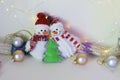 A pair of toy cheerful snowmen with a Christmas tree toy, decor on a light background with illumination