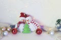 A pair of toy cheerful snowmen with a Christmas tree toy, decor on a light background with illumination