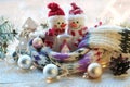 A pair of toy snowmen, a house, a scarf, Christmas decor, illuminations on a wooden surface on a window background Royalty Free Stock Photo