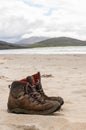 Pair of trekking boots on a remote beach with sea and mountains Royalty Free Stock Photo