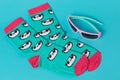 A pair of turquoise socks with a panda face pattern, lie on a turquoise background, near are sunglasses, summer and vacation