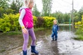 pair of two cute blond caucasian little children brother and sister enjoy have fun playing jumping in dirty puddle