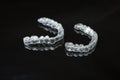 A pair of upper and lower clear retainers or aligners side by side on a dark reflective surface against a black background.