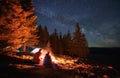 Pair of vacationers sitting near campfire outdoors under stars. Royalty Free Stock Photo