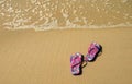 Pair of vibrant colored flip-flops or sandals on golden sand beach with the wave swash Royalty Free Stock Photo