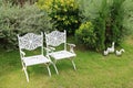 Pair of vintage style white wrought iron chairs in vibrant green garden with duck`s family statues