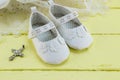Pair of white baby booties on yellow table with lace dress