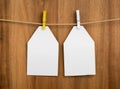 Pair of white carton tags, papers for note, labels for your text or design with clothespins and a rope on a wooden background Royalty Free Stock Photo