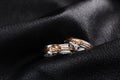 Pair of white gold wedding rings with pink gold knot on black le Royalty Free Stock Photo