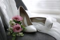 Pair of white high heel shoes, flowers and wedding dress on chair indoors Royalty Free Stock Photo