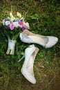 Pair of white ladies shoes on grass and beautiful bouquet of flo