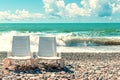 Pair of white plastic deck chairs on pebble beach on sea surf wave background. sunny day summer vacation resort chill Royalty Free Stock Photo