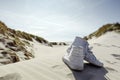 Pair of white sneakers left on sand at beach. Dunes with green grass vegetation Royalty Free Stock Photo