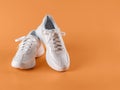 Pair of white tied laces sneakers over an orange background. New unisex chunky sole shoes for active lifestyle, fitness and sports