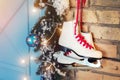 Pair of white vintage leather skates with red laces hanging on old rustic brick wall with garland lights on christmas tree Royalty Free Stock Photo