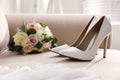 Pair of white wedding high heel shoes and beautiful bouquet on sofa indoors Royalty Free Stock Photo