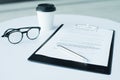 A pair of women`s glasses and a pen lying on top of a white sheet of paper on wooden surface. The sheet has a coffee stain. Copy Royalty Free Stock Photo