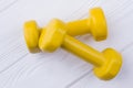 Pair of yellow dumbells on white wood background.
