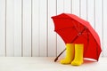 A pair of yellow rain boots and a umbrella on white wooden background Royalty Free Stock Photo