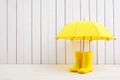 A pair of yellow rain boots and a umbrella on white wooden background