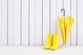 A pair of yellow rain boots and a umbrella on white wooden background