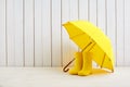 A pair of yellow rain boots and a umbrella on white wooden background