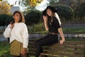 Pair of young beautiful mexican generation y girls. The girl is sitting on the back of the bench, a girlfriend is standing next to