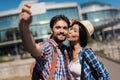 A pair of young tourists makes selfie on the background of a beautiful modern building. The girl kisses the guy. Royalty Free Stock Photo