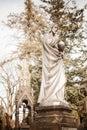 Pale depressive statues, monuments, and gravestones of the cemetery on sunny autumn afternoon. Golden yellow twilight covering the Royalty Free Stock Photo