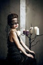 Pale girl with retro style hair in long witch dress with lace face mask in mystical castle