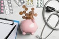 Pale pink ceramic piggy bank with money, stethoscope and pills on white table, flat lay. Medical insurance Royalty Free Stock Photo