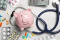 Pale pink ceramic piggy bank, stethoscope, money and pills on white wooden table, flat lay. Medical insurance Royalty Free Stock Photo