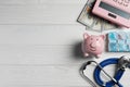 Pale pink ceramic piggy bank, stethoscope and pills on white wooden table, flat lay with space for text. Medical insurance Royalty Free Stock Photo