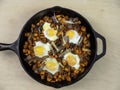 Sweet Potato Hash with Baked Eggs Paleo Diet Meal in Black Cast Iron Pan on Plain Maple Wood Table