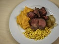 Roasted beef with squash, corn and sauteed onion dinner dish paleo diet meal in a white round plate on plain clean wood table