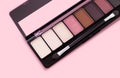 Palette of eyeshadows in brown tones matte and shimmer eyeshadows on a pink background top view. Autumn eyeshadow palette with 8