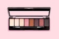 Palette of eyeshadows in brown tones matte and shimmer eyeshadows on a pink background top view. Autumn eyeshadow palette with 8