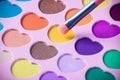 Palette of eyeshadows with multicolor heart-shaped refilles close up. Eyeshadows in macro. Cosmetic brush.