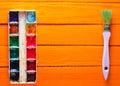 A palette of watercolor paint and a brush for painting on orange wooden boards. Top view. Copy space. Royalty Free Stock Photo