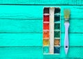 A palette of watercolor paint and a brush for painting on a turquoise wooden boards. Royalty Free Stock Photo