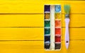 A palette of watercolor paint and a brush for painting on a yellow wooden boards. Top view. Copy space. Royalty Free Stock Photo