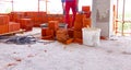 Pallet with heap of red bricks, in background worker builds wall with red blocks and mortar, building site Royalty Free Stock Photo