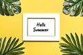 Palm and monstera leaves, orchid, seashells, white photo frame, ship on a yellow background.