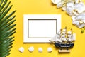 Palm and monstera leaves, orchid, seashells, white photo frame, ship on a yellow background.