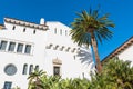 A palm tree and a white Spanish architecture style building with ornate windows and trim under a beautiful blue sky Royalty Free Stock Photo