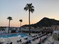 Palm trees against the background of mountains and blue sky. Tall tropical trees on a summer evening at sunset. Swimming pool of Royalty Free Stock Photo