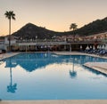 Palm trees against the background of mountains and blue sky. Tall tropical trees on a summer evening at sunset. Swimming pool of Royalty Free Stock Photo